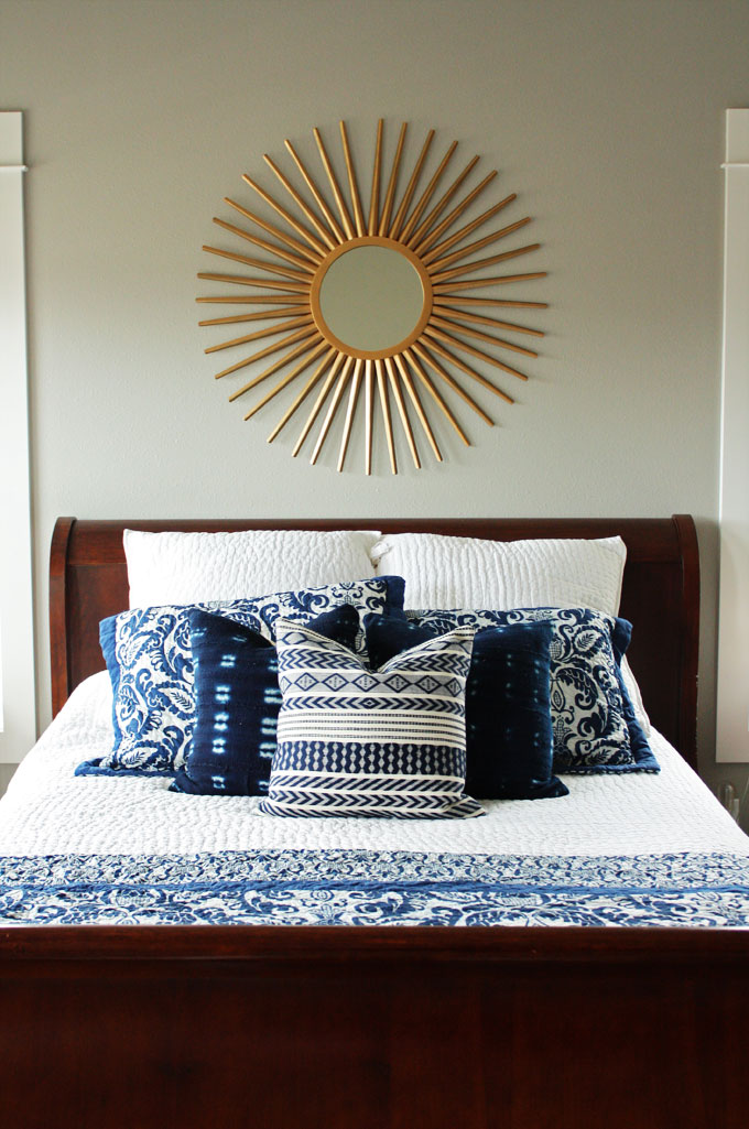 A master bedroom with dark wood furniture, white and navy bedding, and a brass sunburst mirror | modern farmhouse inspiration
